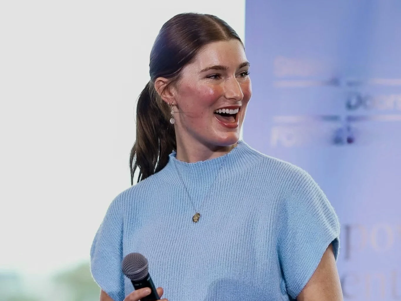 A woman in a light blue knitted top, holding a microphone