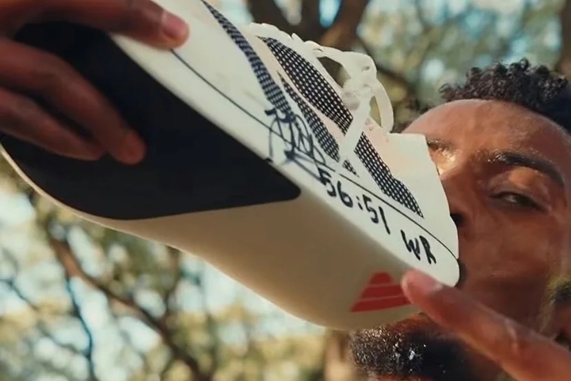 A young man with dark hair and a beard kisses a running shoe.