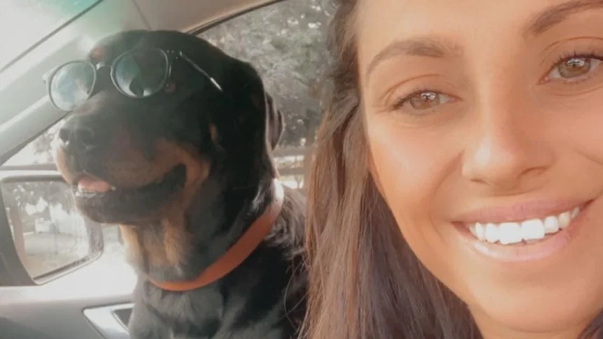 Marina, smiling young woman takes a selfie while sitting in a car next to a dog wearing sunglasses.