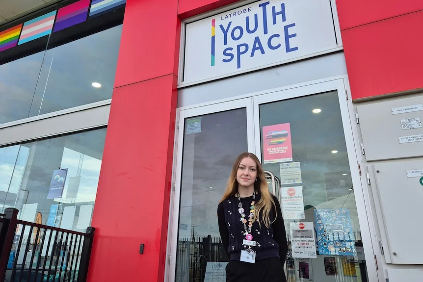 A young woman with long strawberry blonde hair in a dark top stands outside a colourful building with a Latrobe Youth Space sign