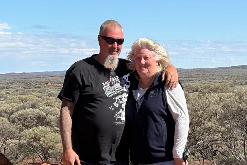 A man and a woman stand in a landscape environment smiling at the camera.