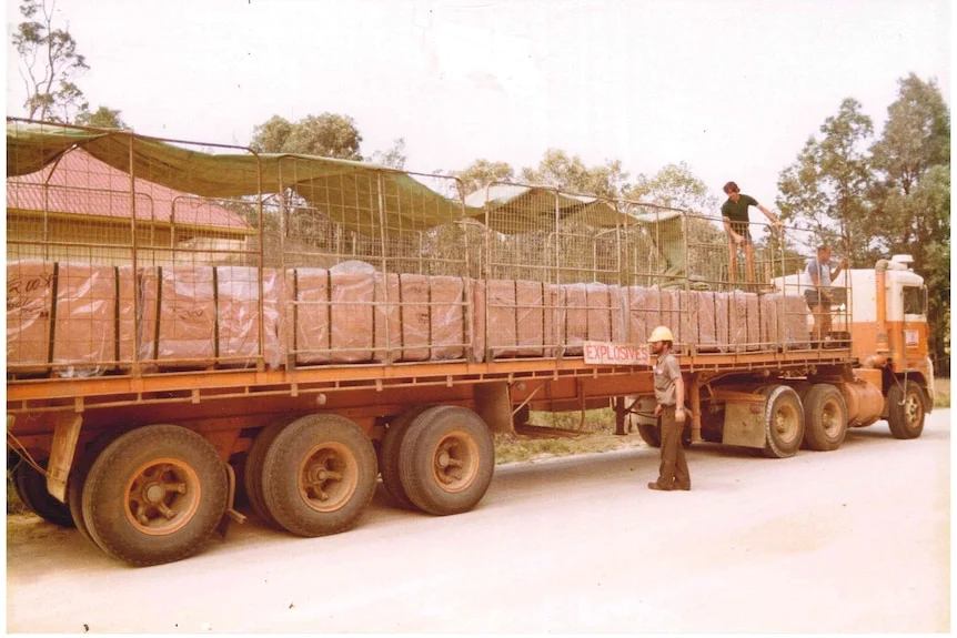 A old grainy photo of a long flat-bed truck loaded with crates with a person beside it and on top.