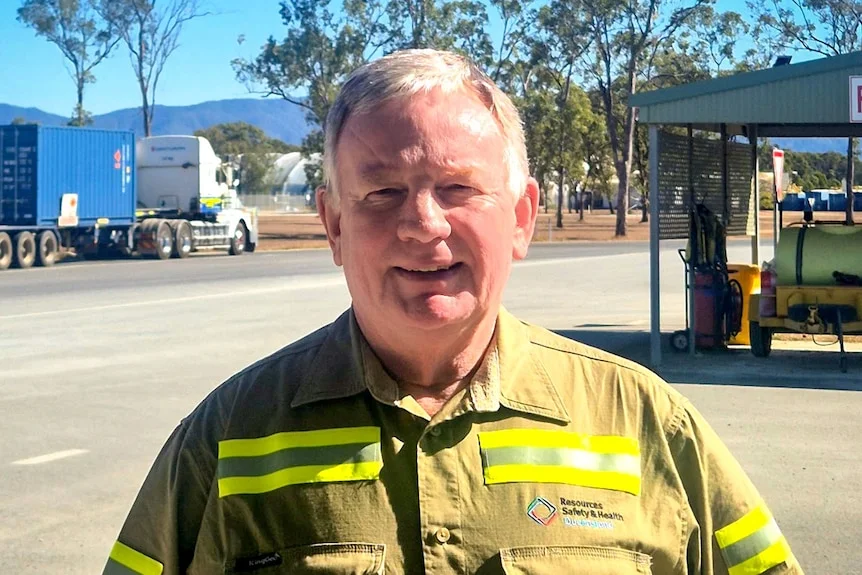 A man in a high vis shirt smiling in front of buildings.