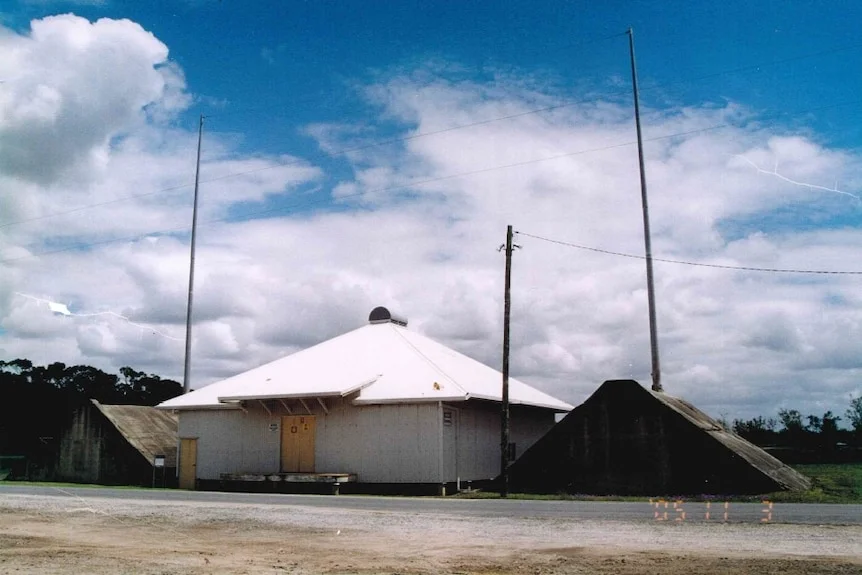 A grainy photo of an old small house-like structure between two metal pyramid-looking structures.