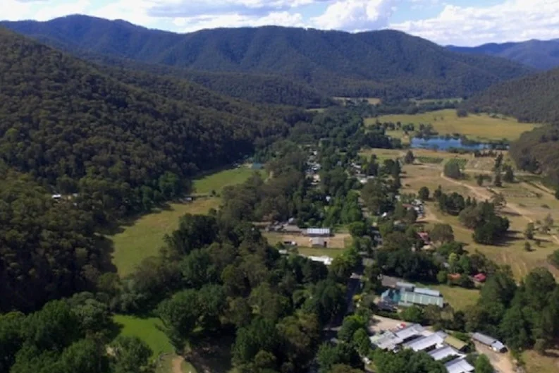 A drone picture looking down on a town in an alpine valley, with a dredge hole in the background. 