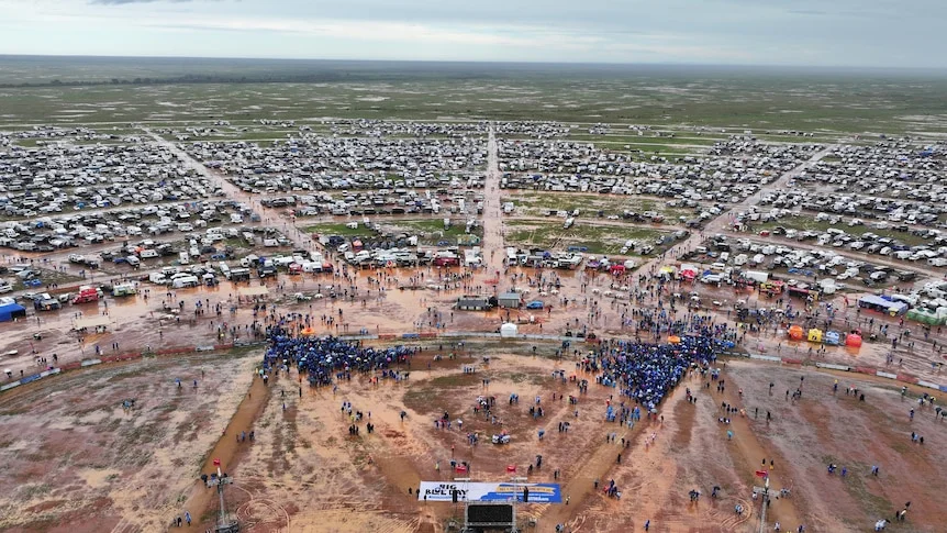 Crowd of caravans parked around a stage and festival site where people wearing blue are gathered. 