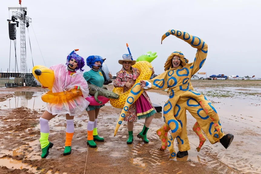 Four people in fancy dress stand in large muddle at an outback music festival