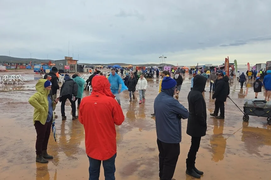 People walking around at festival site with muddy puddles and water wearing rain gear 
