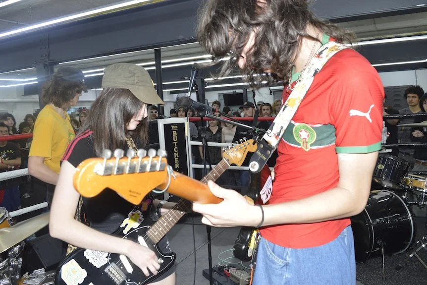 three poeple play guitars inside a boxing ring as part of a diy show