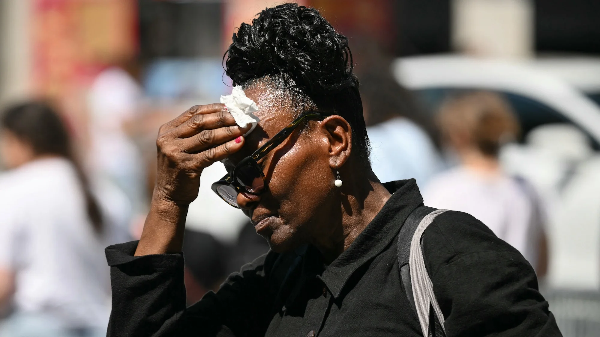 An older woman mops her head with a tissue in hot weather