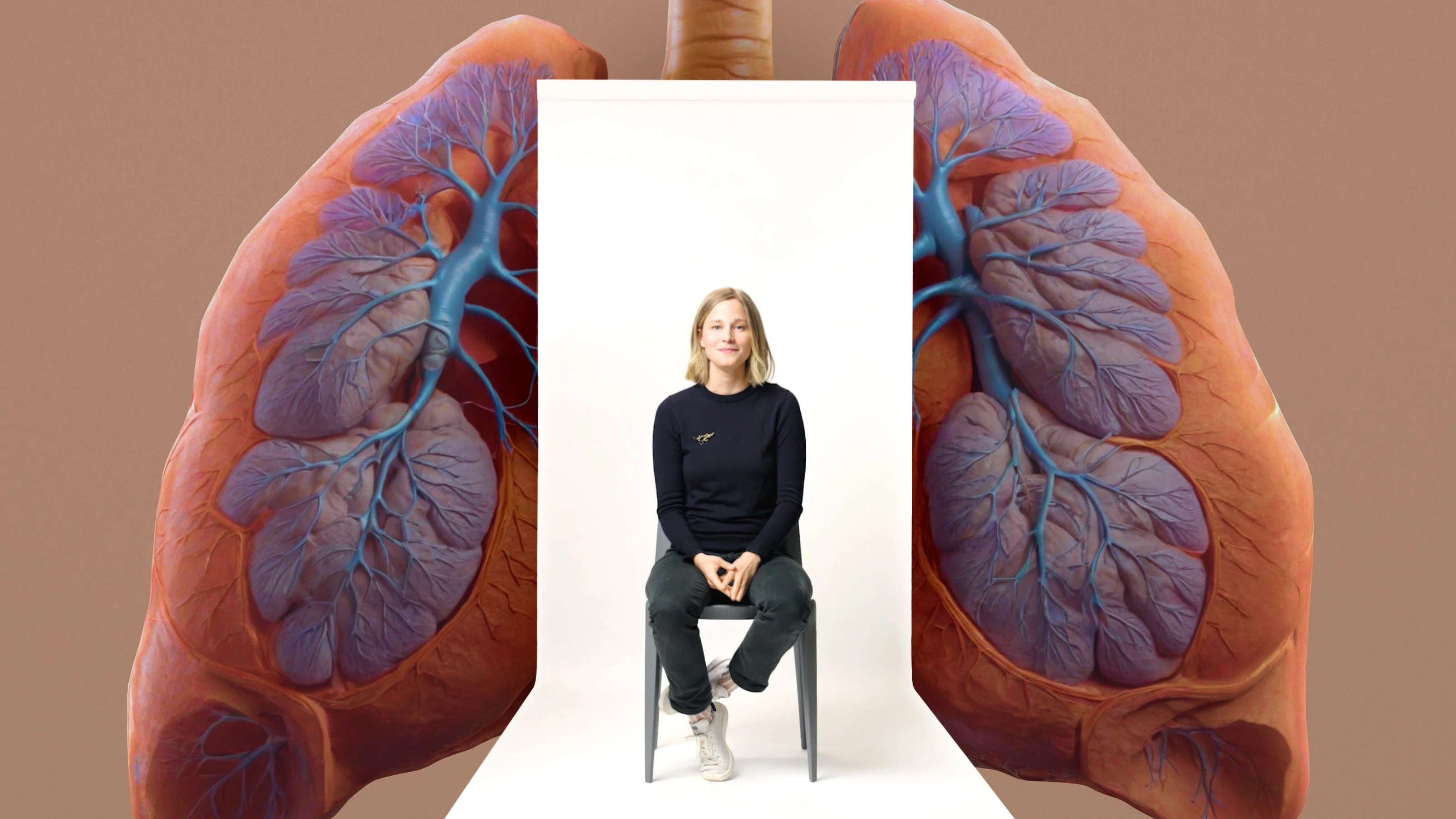 A person sits on a chair in front of an illustration of human lungs, highlighting the branching bronchial tubes and lung tissue in detail.