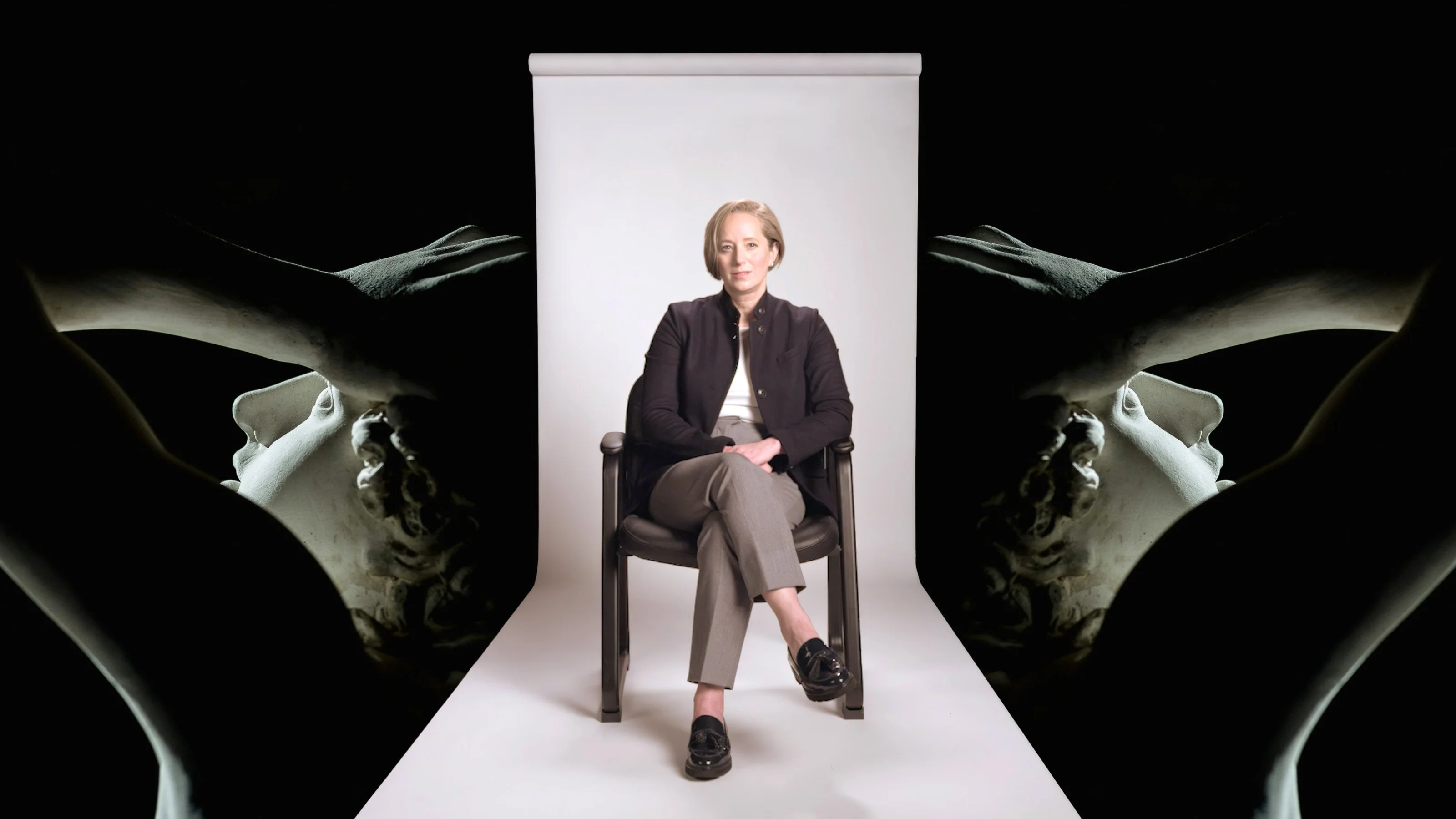 A person in business attire sits on a chair against a white backdrop, flanked by artistic black-and-white images of sculptures and a person’s outstretched arms.