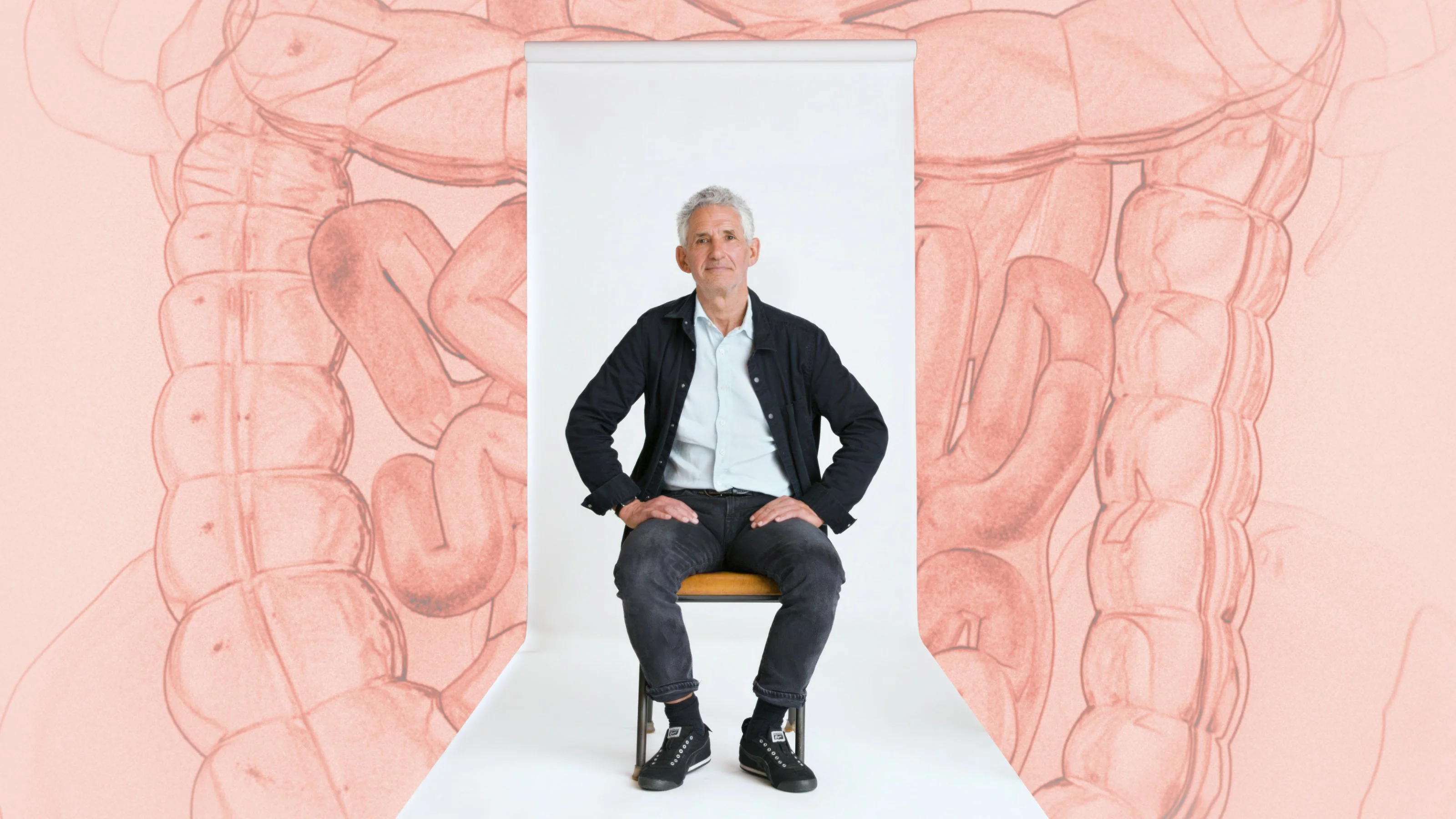A man with gray hair sits on a stool against a white backdrop, framed by an illustration of the human digestive system in shades of pink.