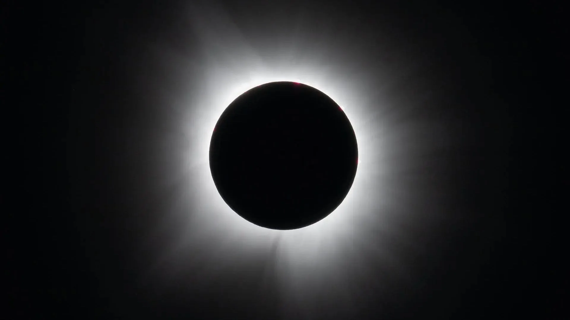 A black circle against a black background surrounded by white wispy tendrils