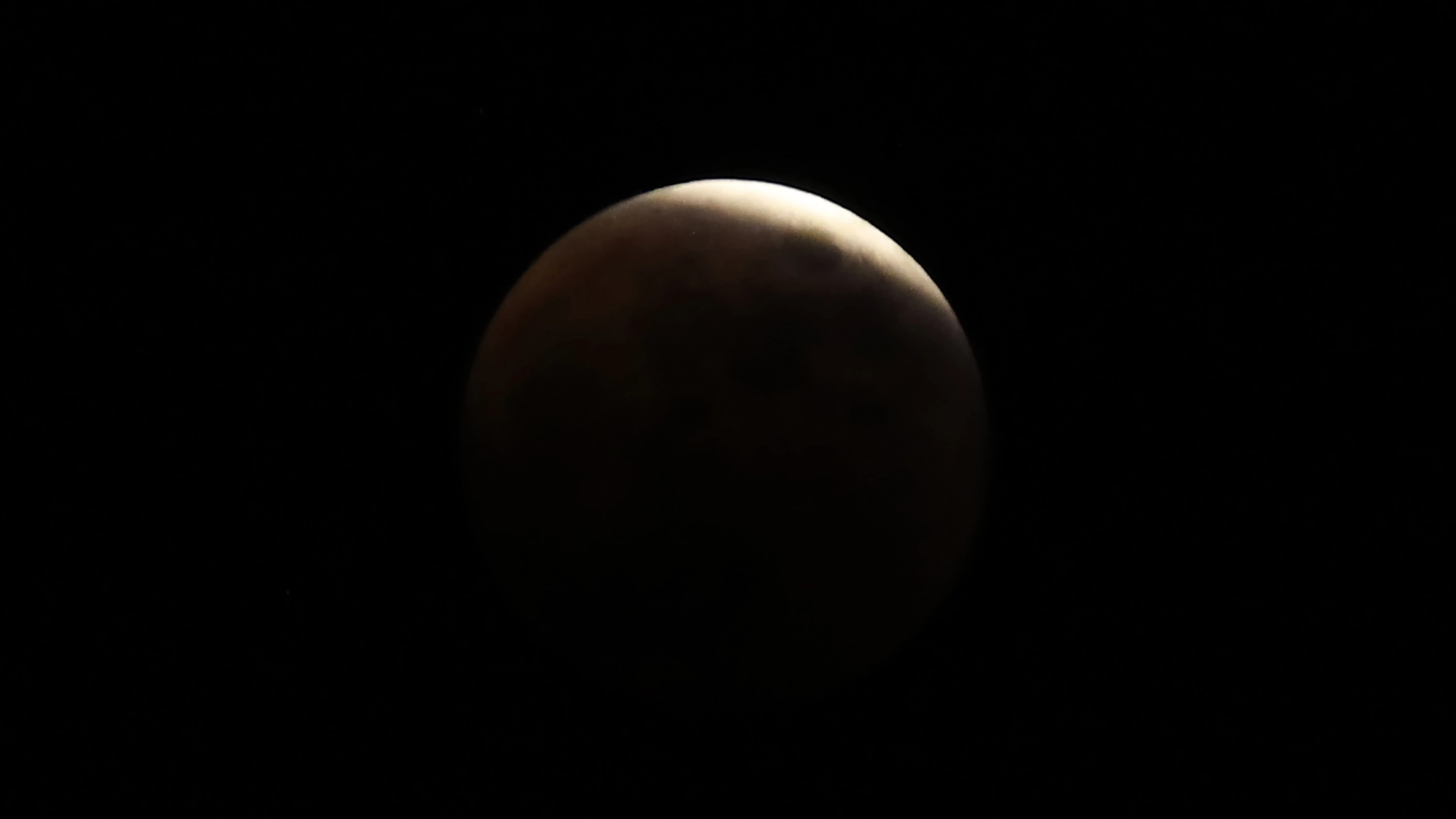 a barely illuminated moon with just one little bright sliver of light at the top