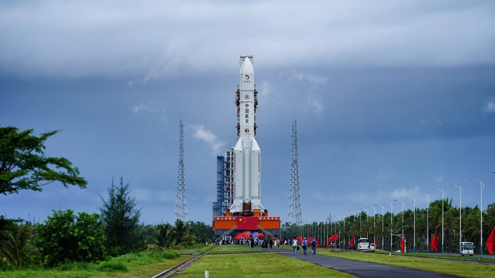 a white rocket upright on a launch tower surrounded by green, tropical trees