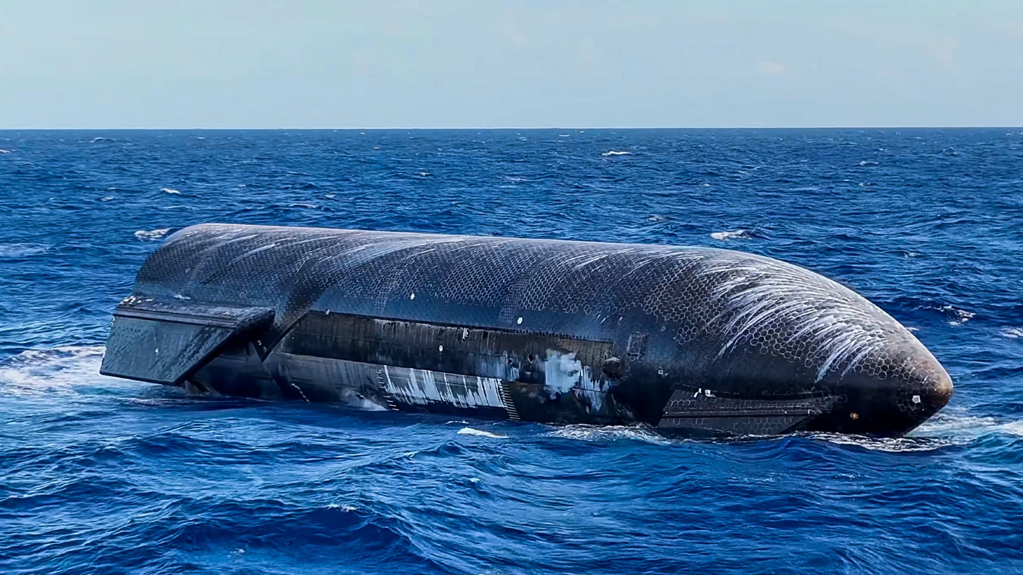 a large black cylinder with wing-like canards floats on top of a choppy blue sea
