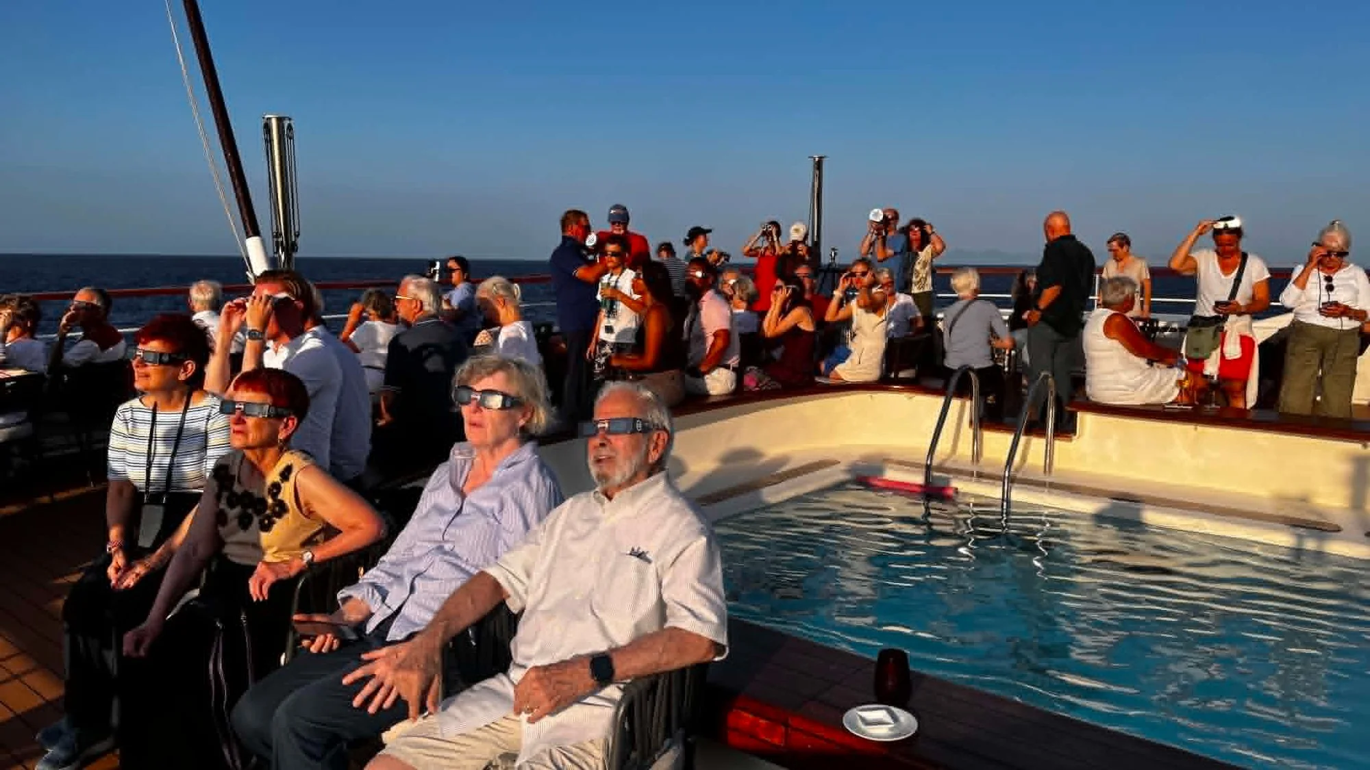 people sit on the deck of a ship wearing paper sunglasses, looking skyward
