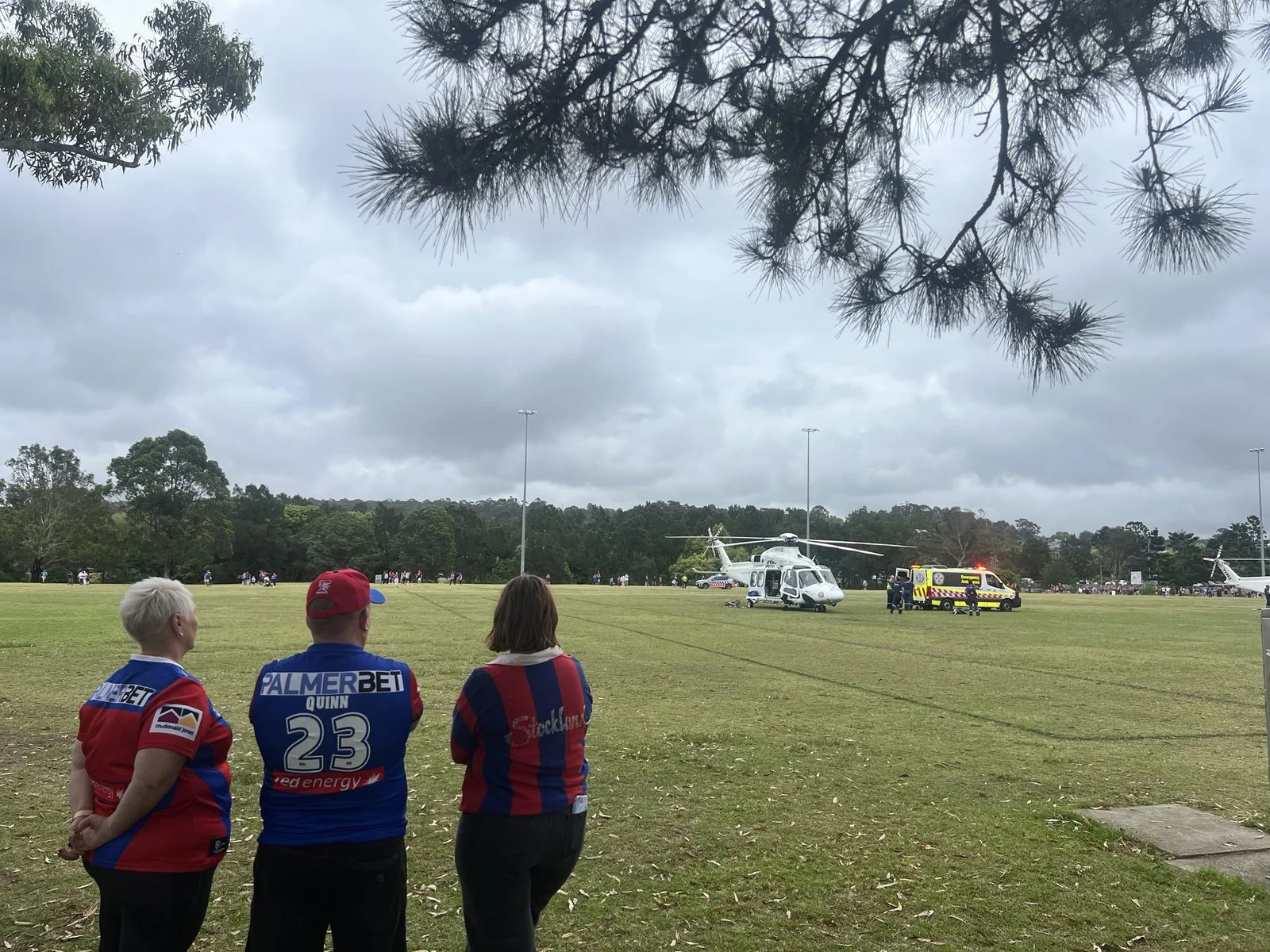 Three people in Newcastle Knights jerseys look at a helicopter standing on a field