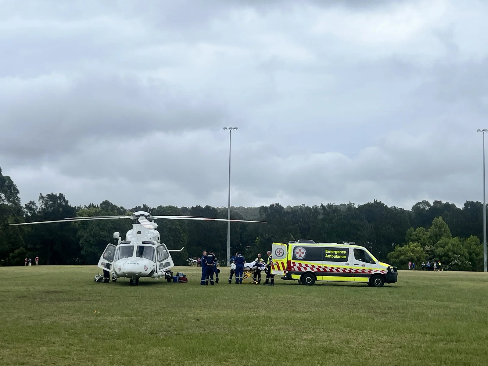 A helicopter and an ambulance parked on a grassy field, a person can be seen on a stretcher