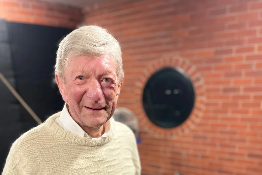 A man wearing a jumper smiles at the camera.
