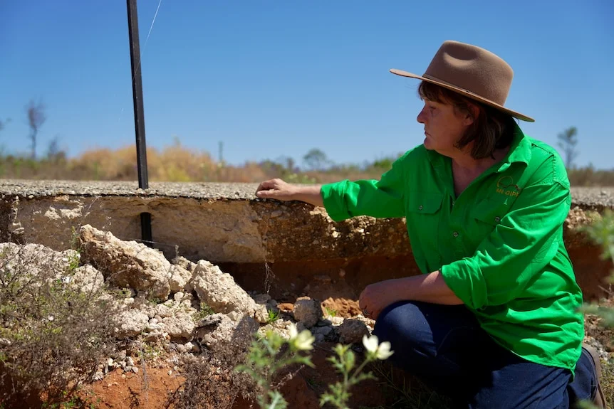 Mt Gipps station owner Sam Maiden wearing green shirt and a hat on side of road staring at part of road eroded away. 