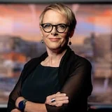 A woman with glasses stands in a TV studio.