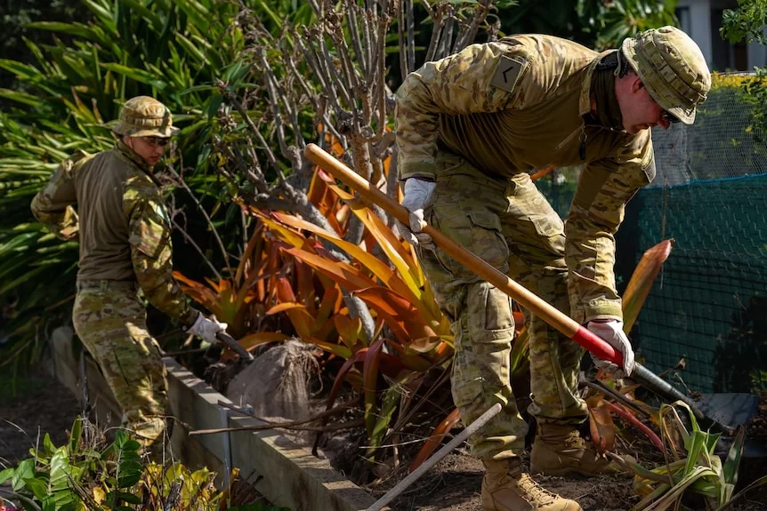 Two soldiers in fatigues at work digging out a garden bed.