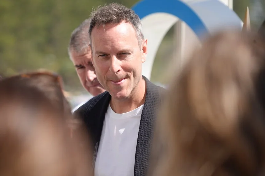 Brisbane 2032 chief marketing officer Brent Hill in front of the Olympic rings with a group of people.