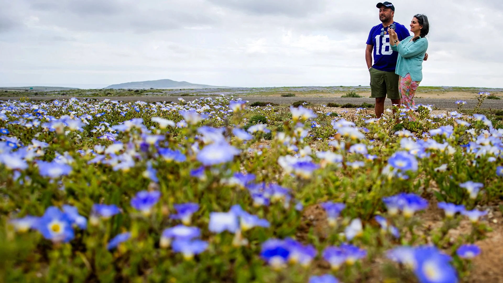 Two people stand in a patch of purple flowers.