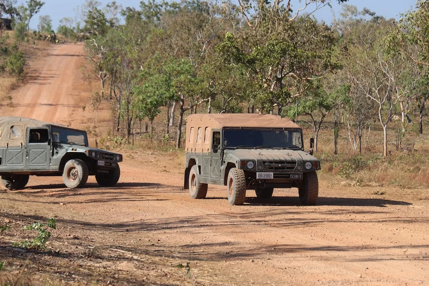 A troop carrier painted in camouflage drives up a dusty dirt road