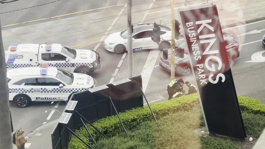 Police cars block a street near where officers bend over a preson on a city street corner.