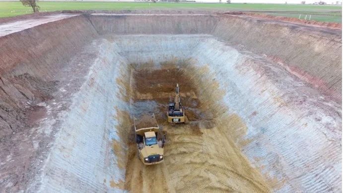 green paddock with a sandy mine pit about 25 meters deep with two yellow earthmoving trucks.
