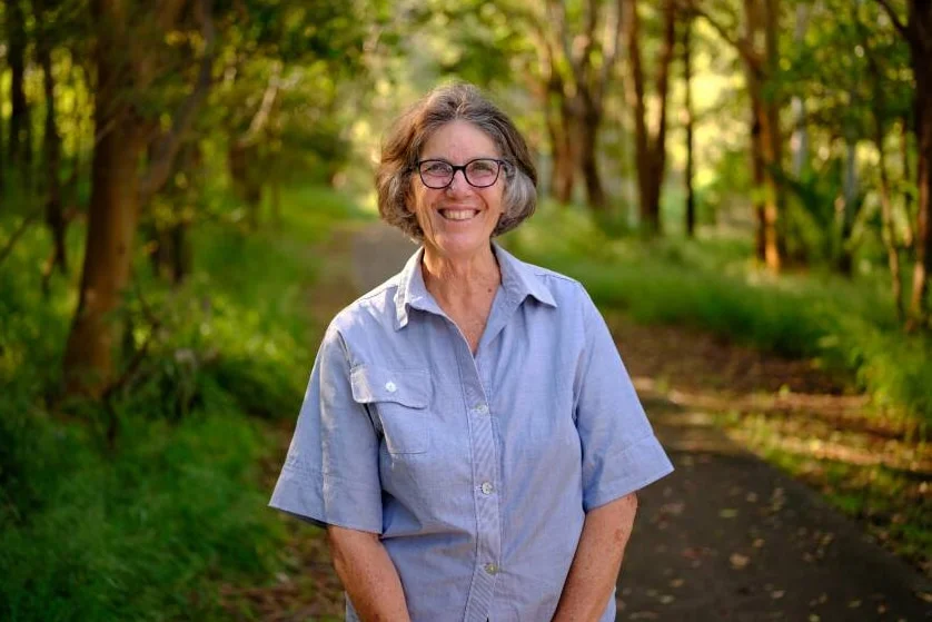 Wendy Wales stands near trees, smiling at the camera.