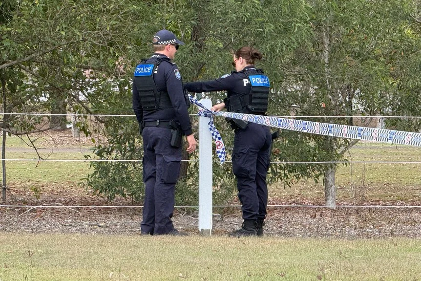 Police officers examine a fence line near a crime scene.