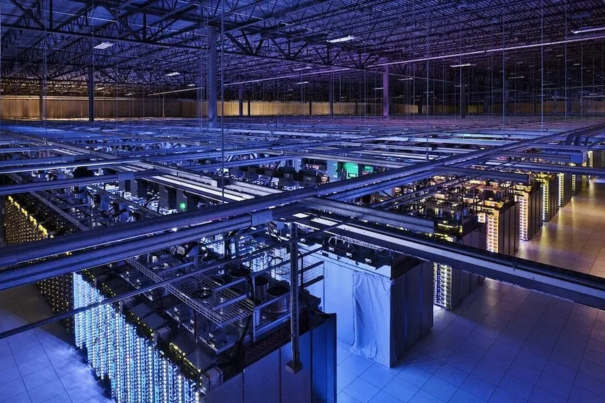 The dimly lit inside of a large warehouse looking down at rows of server racks.