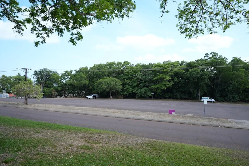 Two cars on an empty lot, typically used for overflow parking but a pink sign indicates it's the site of a proposed development.