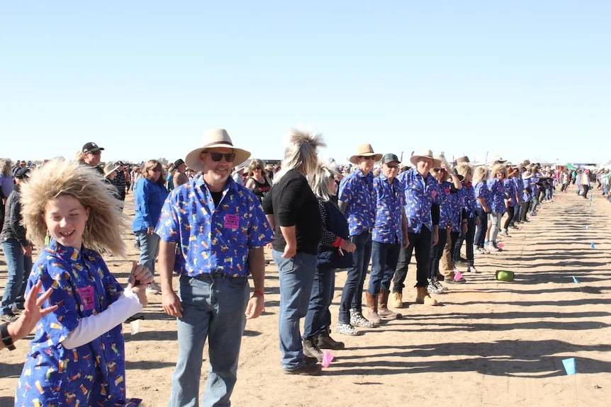 A row of people pre[are to do a dance at an outback festival