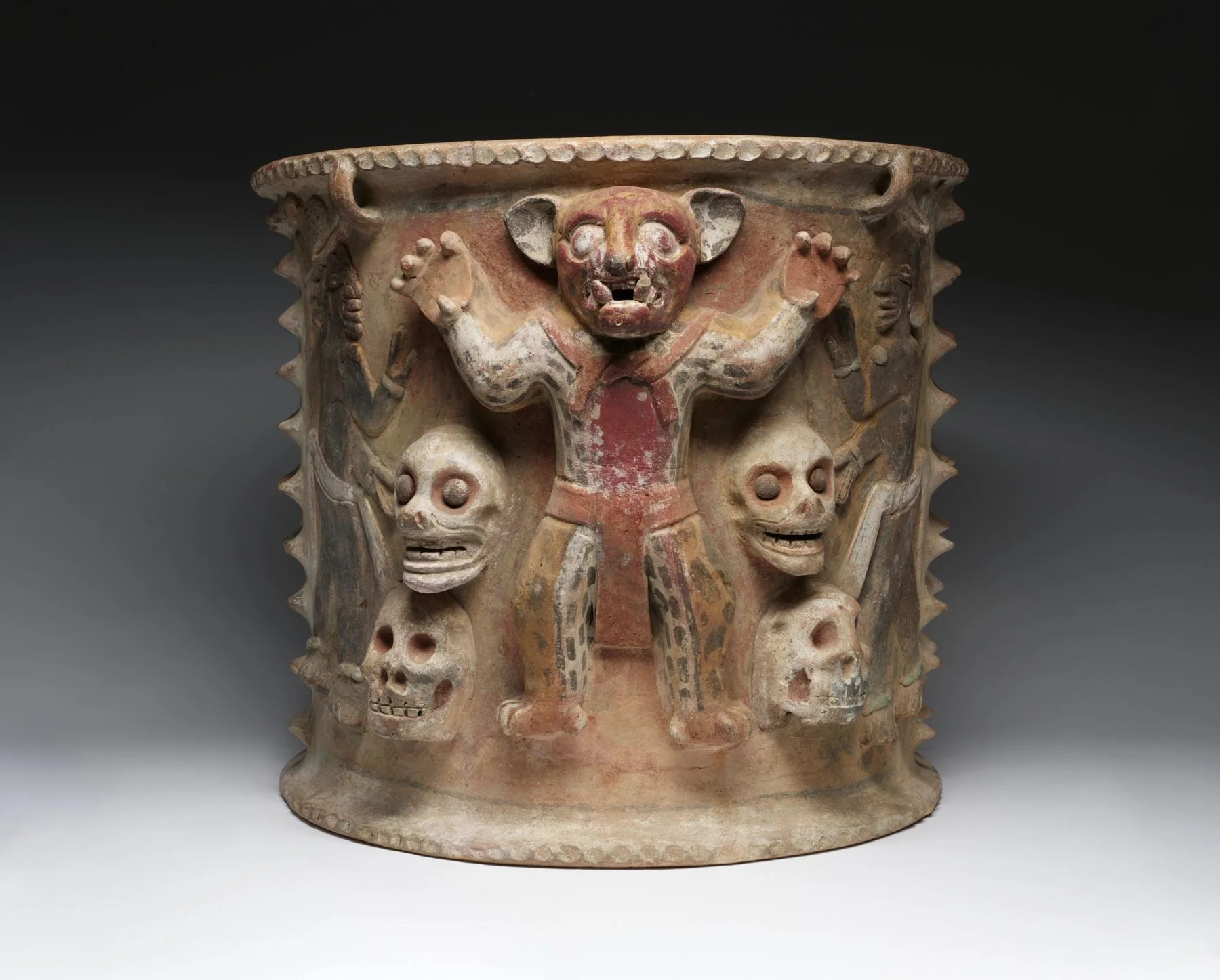 a ceramic urn depicting a person wearing a jaguar costume surrounded by four human skulls