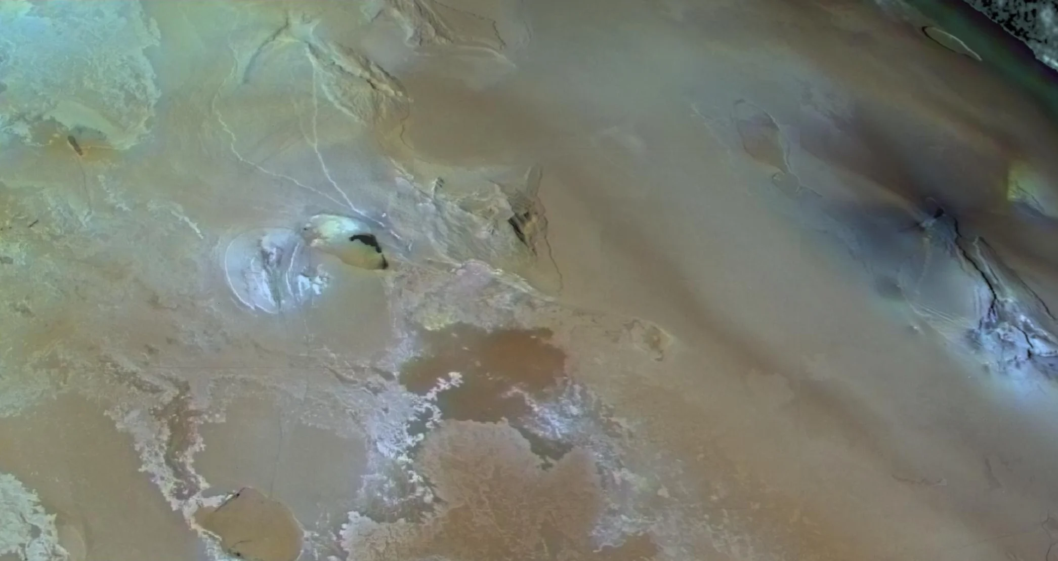Aerial view of a desert landscape with sandy textures, faint patches of color, and subtle ridges reminiscent of Olympus Mons, the highest mountain in the solar system.