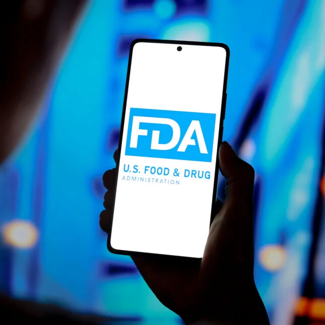 Stock photo of The FDA logo displayed on the screen of a smartphone with blue and black background
