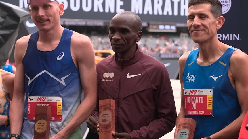 The three runners stand together and hold their trophies.