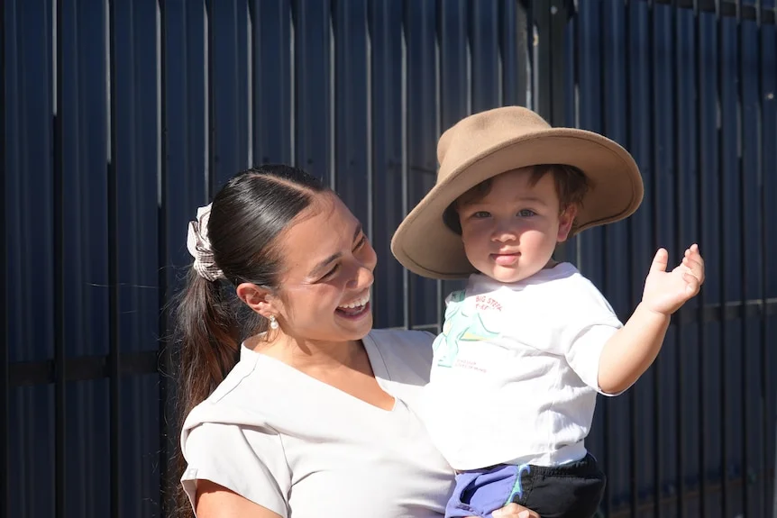 baby thomas ibelli wears an akubra-style hat being held by his smiling mum