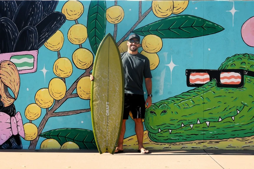 pro surfer holding green surfboard in front of mural with crocodile