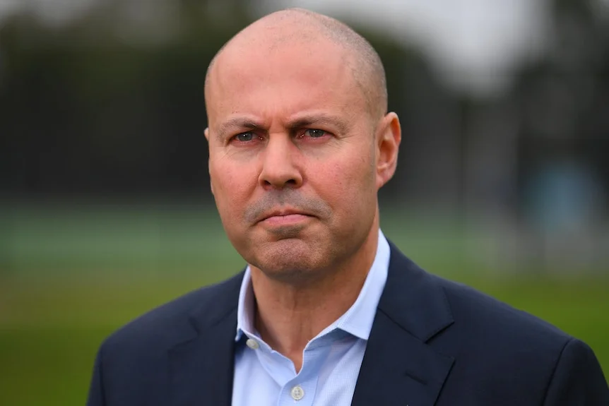 Josh Frydenberg wears a navy jacket and a light-blue collared shirt. He has a serious expression.
