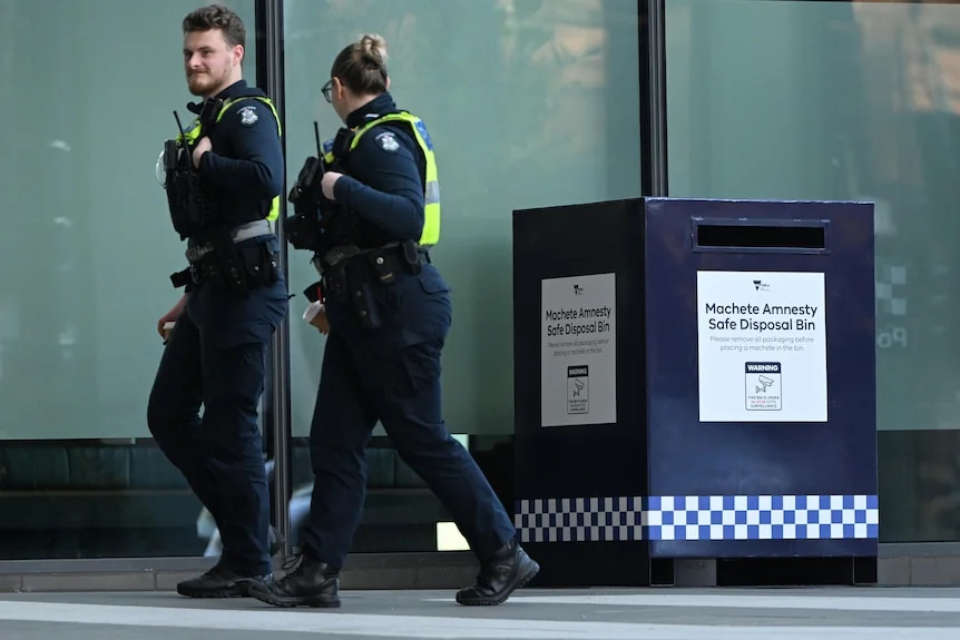 Two police officers walk away from a Victorian machete amnesty safe disposal bin.