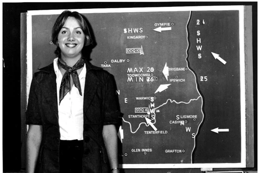 Black and white photo of Woodward standing in front of a map of Queensland and northern NSW with weather information stuck on.