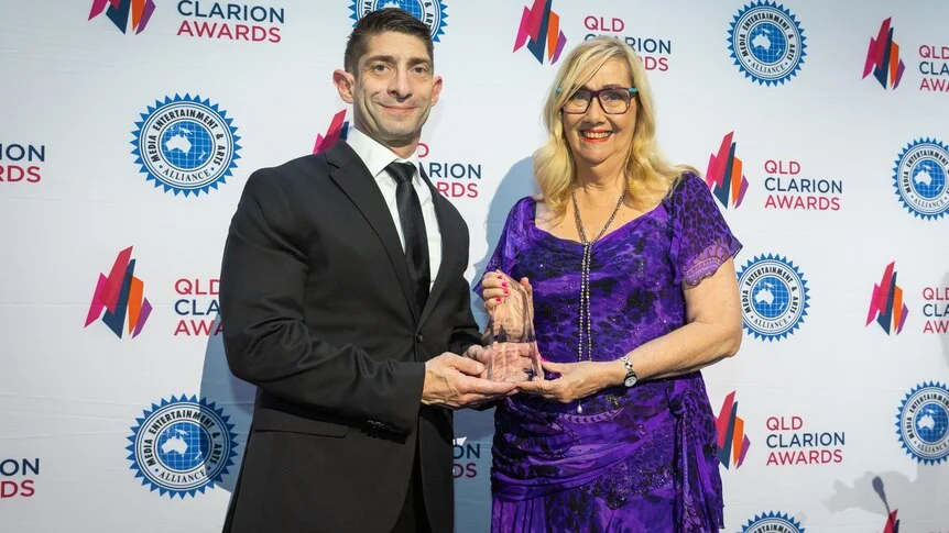 a woman in a purple dress holding a trophy beside a man in a suit