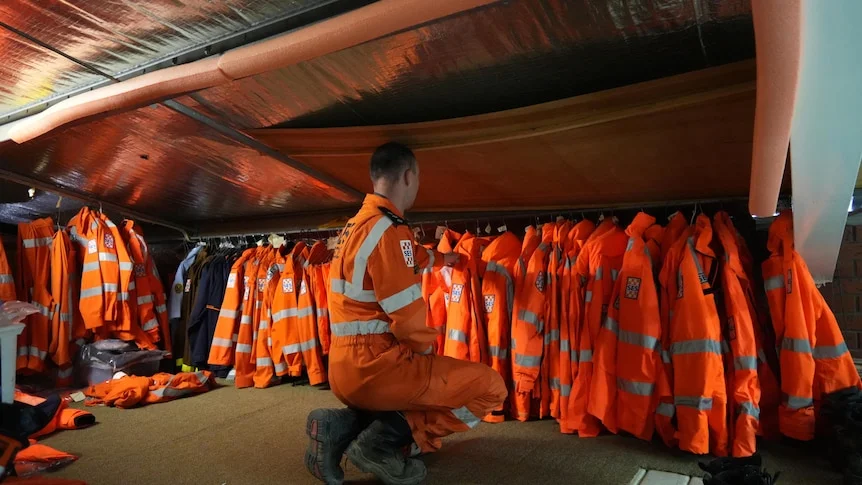 A man in SES uniform kneeling down in front of a row of SES uniforms