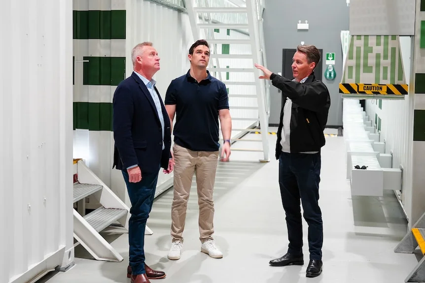 Three men in a white building, gesturing.